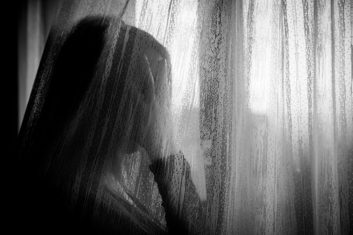 Ensam ledsen kvinna stirrandes ut genom fönster.