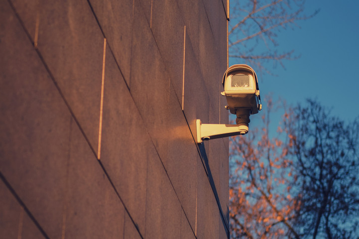 Övervakningskamera fäst på fastighet. Närbild med vy över urbant område under solnedgång.