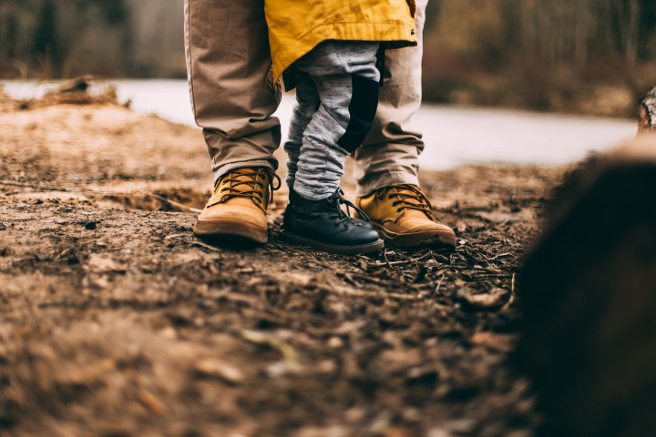 Förälder och barn med boots i fokus ståendes i skogsmiljö.