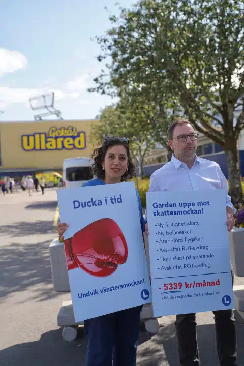 Simona Mohamsson, partiledare Liberalerna, och Fredrik Malm, utrikespolitisk talesperson, håller upp skyltar som visar varför L:s politik ger mer pengar i månaden till en barnfamilj än V:s politik.